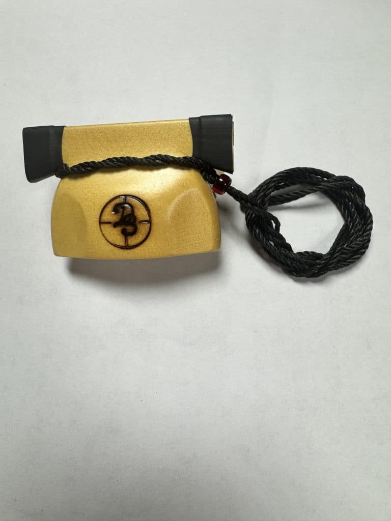 Yellow Cedar Bell Call hand-turned deer call with black ends and red bead cord detail.